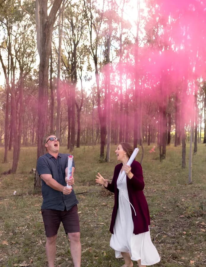 Courtney and her husband at a gender reveal, pink smoke rising through the trees
